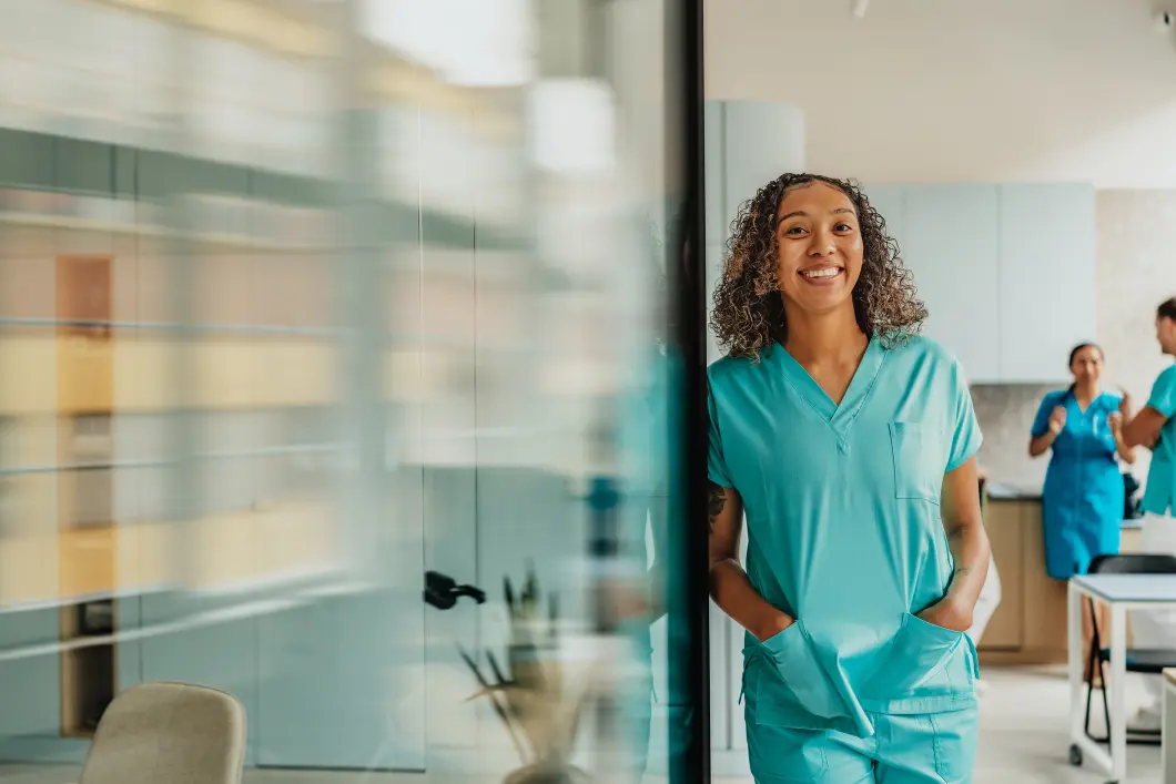 Smiling nurse in scrubs, standing in clinic.